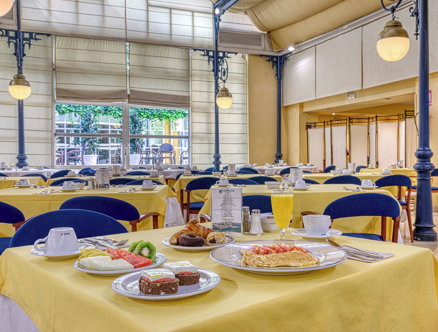 A dining area with tables set for breakfast, featuring a variety of food items and a menu sign.