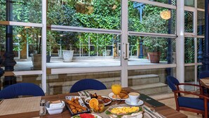 Una mesa de desayuno servida con platos de comida, un frutero y un vaso de jugo de naranja.