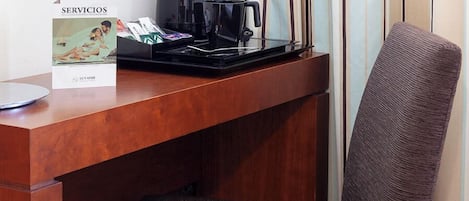 Habitación de hotel con escritorio de madera, una silla, lámpara, cafetera y cartel con información sobre los servicios.