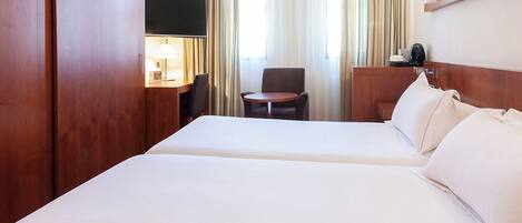 A hotel room with two beds, a desk with a lamp, a chair, and a TV.