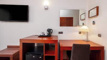 Hotellihuone, jossa on puinen työpöytä, tuoli, televisio, peili ja lamppu.