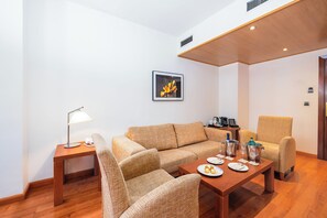 Una sala moderna con un sofá, sillones, una mesa de centro de madera y una mesita auxiliar con una lámpara.