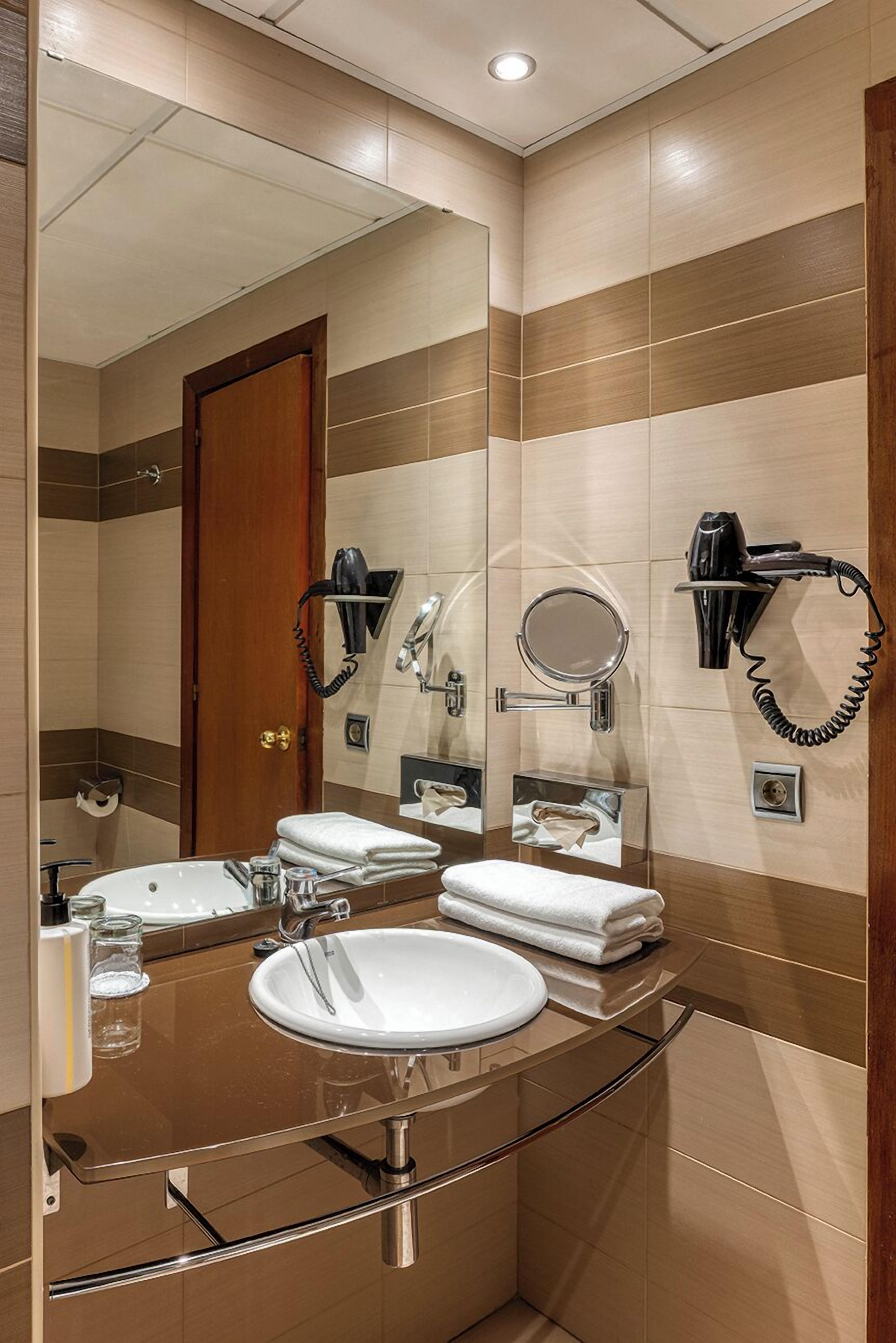 Une salle de bain moderne avec un grand miroir, un lavabo et deux sèche-cheveux fixés au mur.