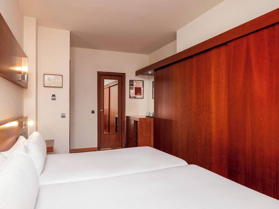A hotel room with a large bed, wooden wardrobe, and a mirror.