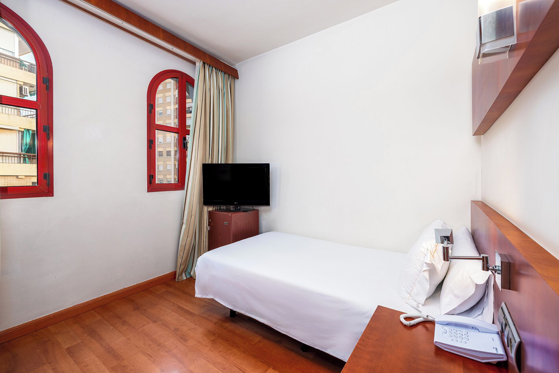 Habitación de hotel con cama, televisión, teléfono y ventana con cortinas.