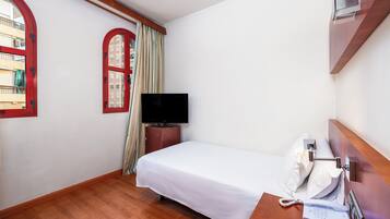 Habitación de hotel con cama, televisión, teléfono y ventana con cortinas.