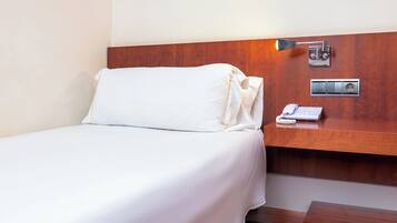 Une chambre d’hôtel comprenant un lit, une table de chevet avec un téléphone et une prise électrique, ainsi qu’un luminaire fixé au mur.