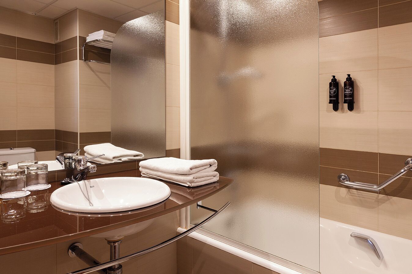 A modern bathroom with a round sink, a glass shower enclosure, and a handrail.