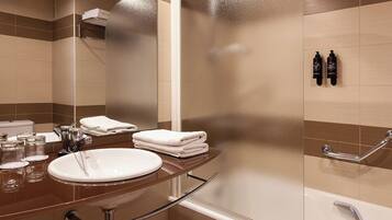 A modern bathroom with a round sink, a glass shower enclosure, and a handrail.