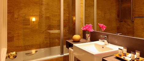 Un baño moderno con ducha de vidrio, lavabo blanco y tocador con artículos de aseo.