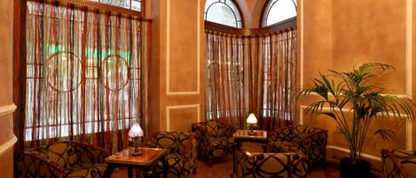 A lobby with patterned chairs, a table with a lamp, and a potted plant.