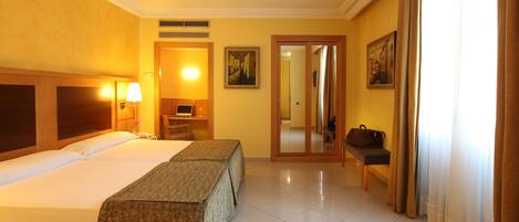 A hotel room with two beds, a desk, a chair, a lamp, a painting, and a mirror.