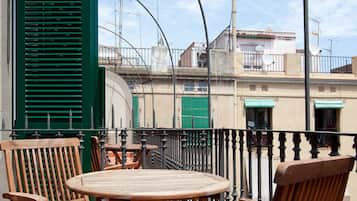 Un balcón con mobiliario de madera y vistas a edificios al fondo.