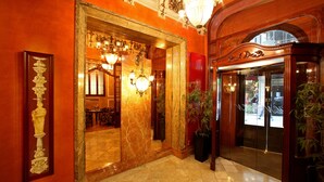 A grand lobby with marble flooring, ornate chandeliers, and a large mirror reflecting the interior. - Hotel Nouvel (Barcelona)
