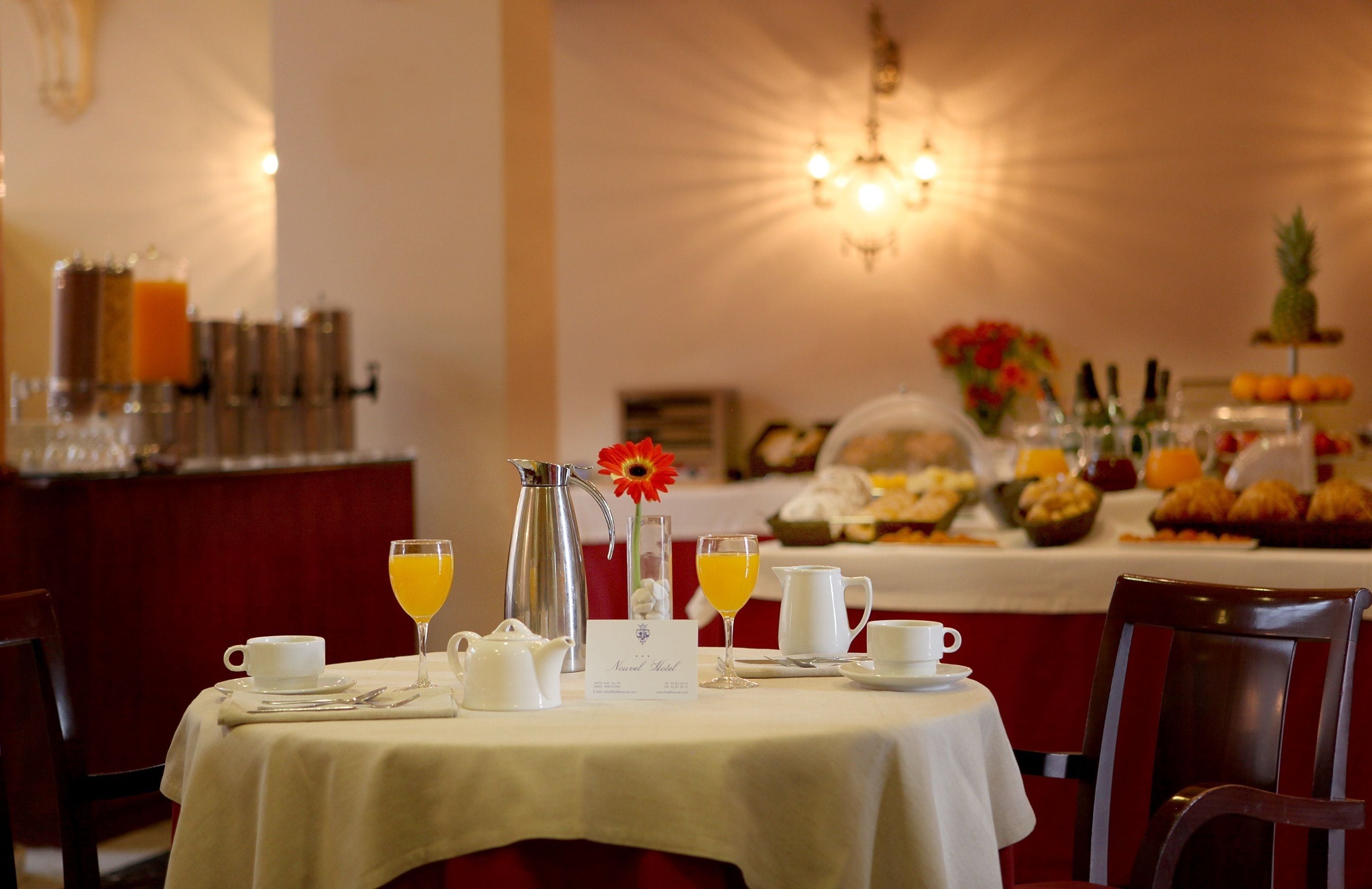 A breakfast setting with a table set for two, including a pitcher, teapot, cups, and a glass of orange juice.