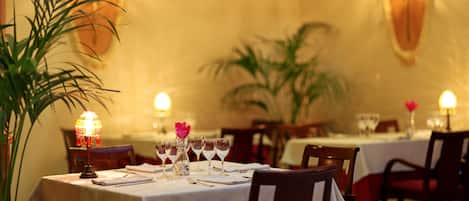 Un restaurante con mesas dispuestas para comer, que destaca por su ambiente cálido con luces de pared y plantas en macetas.