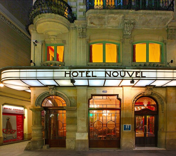 The exterior of the HOTEL NOUVEL with a classic facade, large arched entrance, and illuminated signage. - Hotel Nouvel (Barcelona)