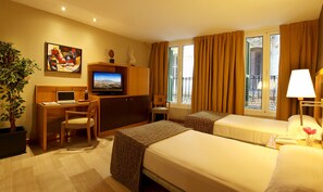 A hotel room with two beds, a desk with a laptop, a television, a potted plant, and a window with curtains. - Hotel Nouvel (Barcelona)