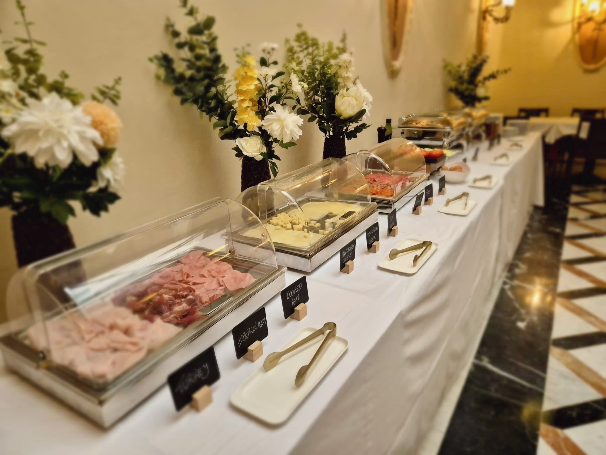 Buffet amb diferents aliments en recipients transparents, etiquetats amb noms com 'Turkey' i 'Cheese'.