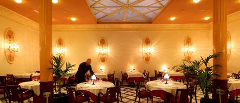 A dining area with round tables, chairs, and chandeliers.