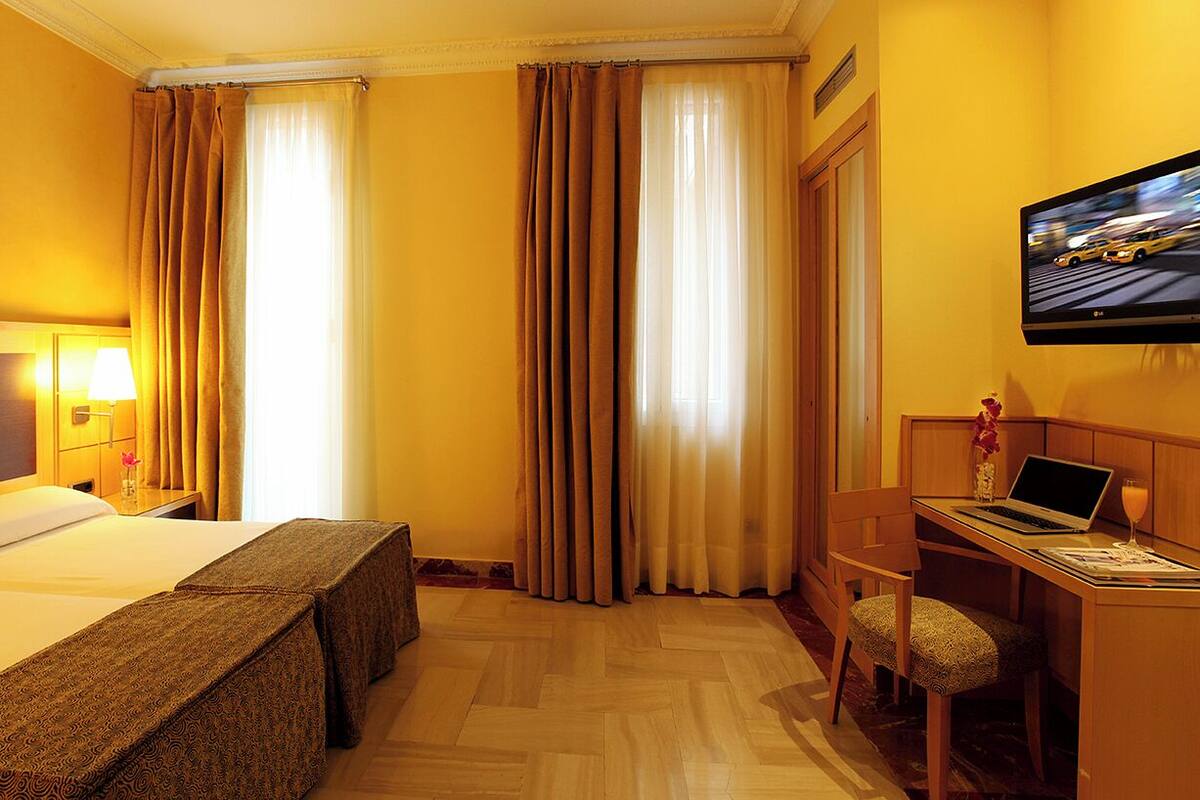 A hotel room with a bed, a desk, a chair, a TV, and curtains.