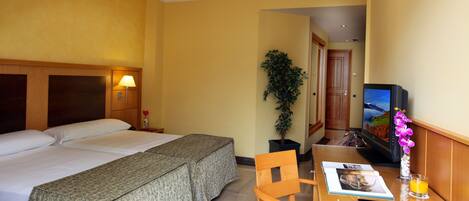 A hotel room with two beds, a desk with a chair, a television, and a potted plant.