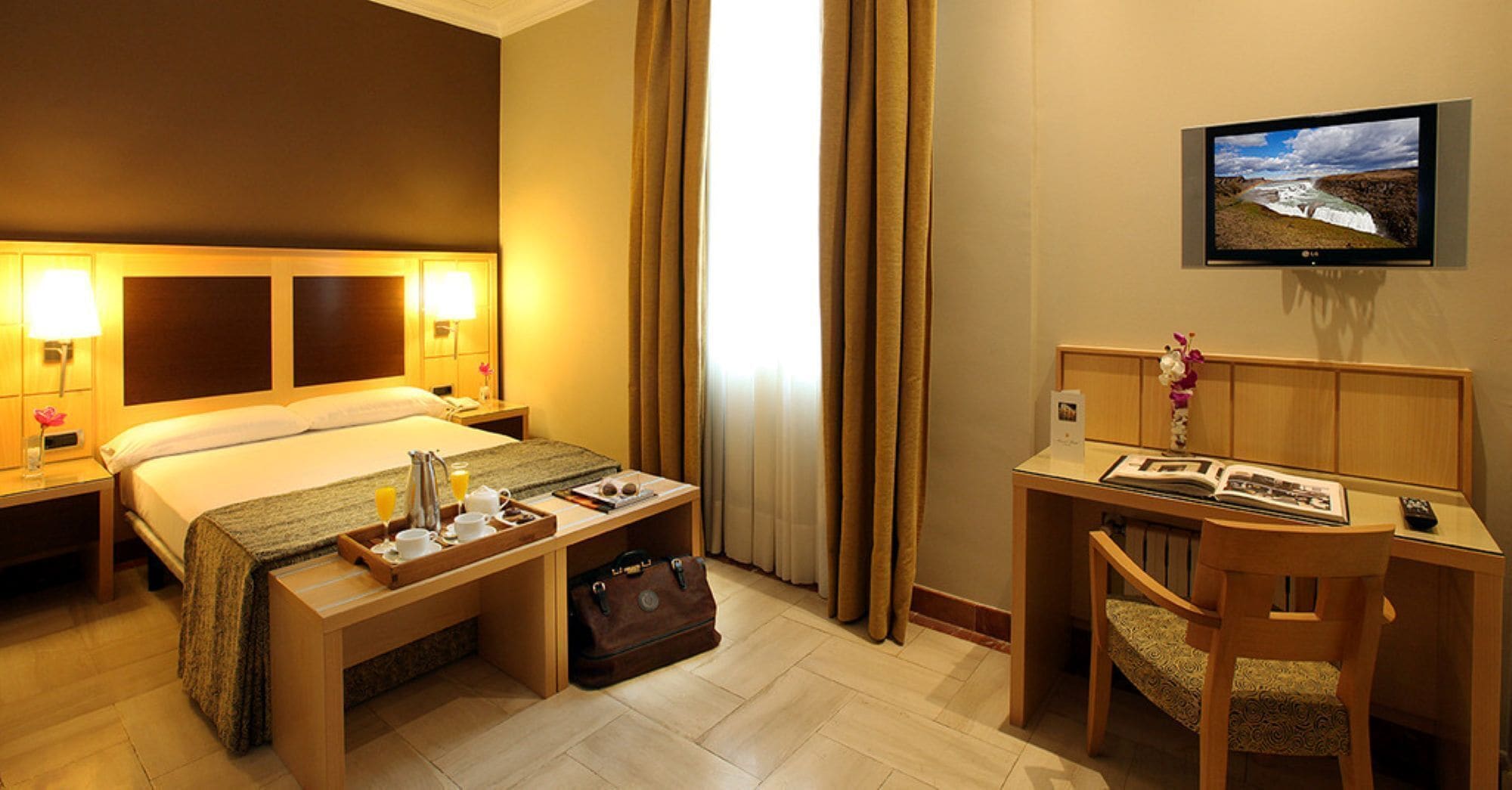 A hotel room with a bed, bedside tables, a desk, a chair, a TV, and curtains.