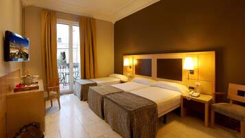 Habitación de hotel con dos camas, televisión, minibar y vistas al balcón exterior.