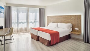 A modern hotel room with a wooden headboard, a large bed with a red blanket, a wooden desk, and a view of the outdoors through sheer curtains. - Hotel VM Prisma (Escaldes-Engordany)