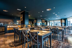 Un restaurante espacioso con varias mesas y sillas, una zona de bar y vistas a la ciudad a través de amplios ventanales.