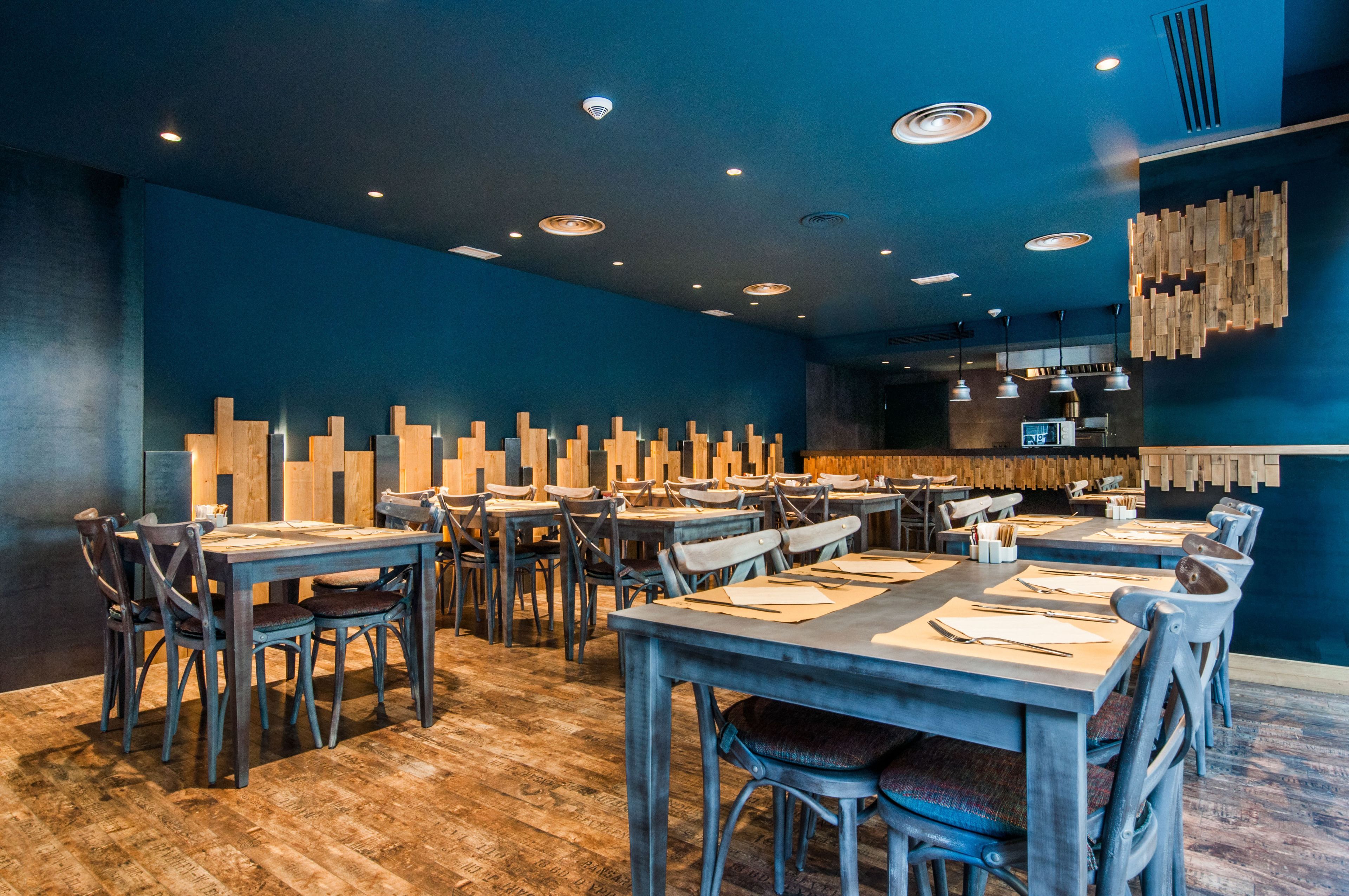 A restaurant with wooden tables and chairs, a blue wall, and a wooden wall decoration.