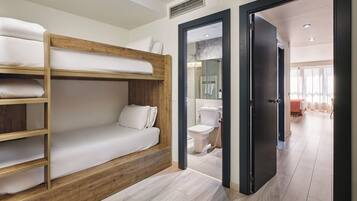 Habitación con literas, cabecera de madera, baño con inodoro y lavamanos, y una puerta que da a otra habitación.