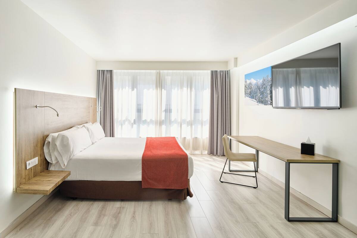 Ein modernes Hotelzimmer mit Bett, Schreibtisch und Fernseher.