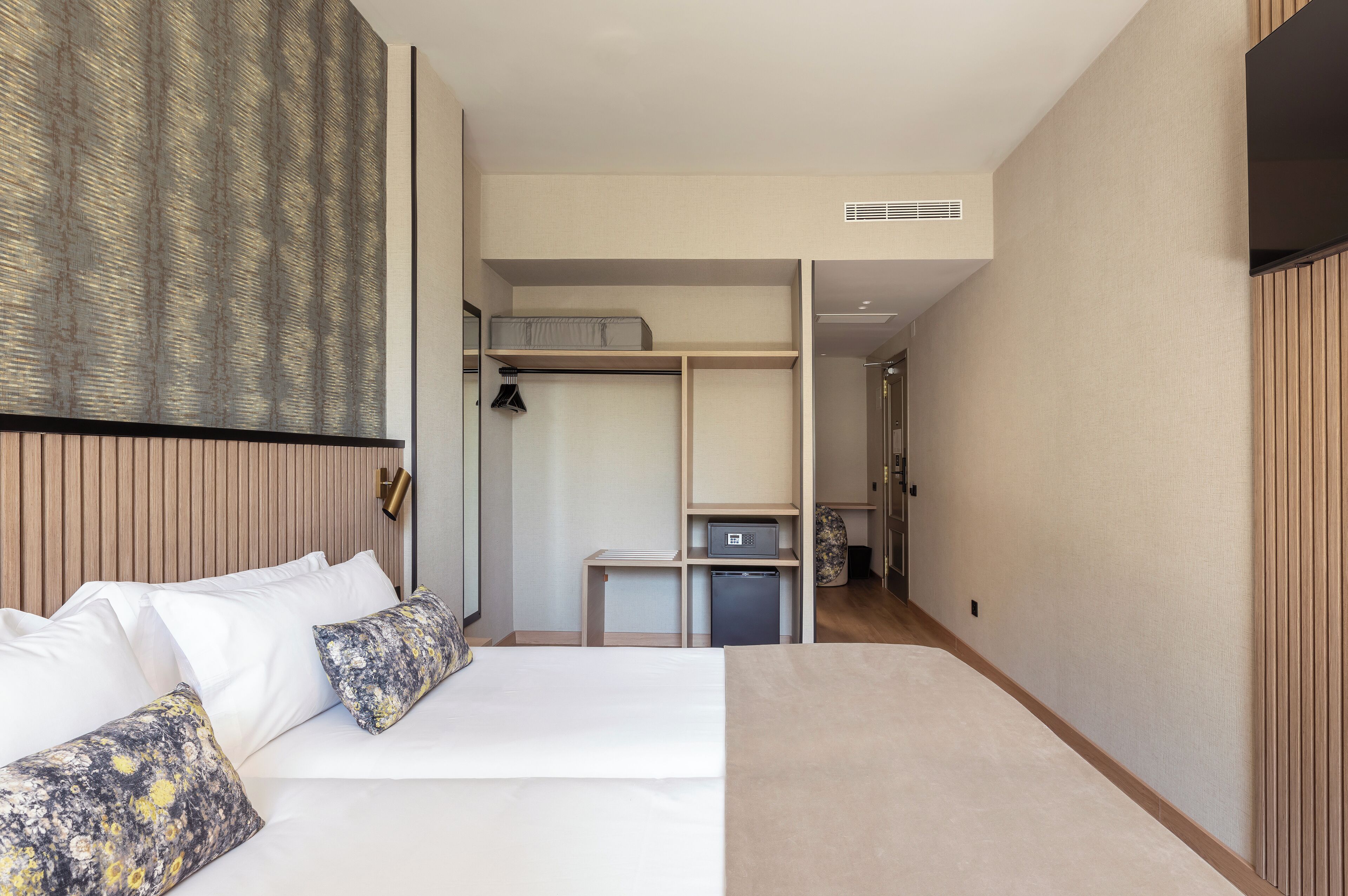 Una habitación de hotel moderna con una cama grande, un armario, un escritorio y una pequeña kitchenette.