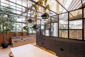A modern dining area with a long table, chairs, hanging pendant lights, and potted plants. - Hotel Acta Piramides (Madrid)