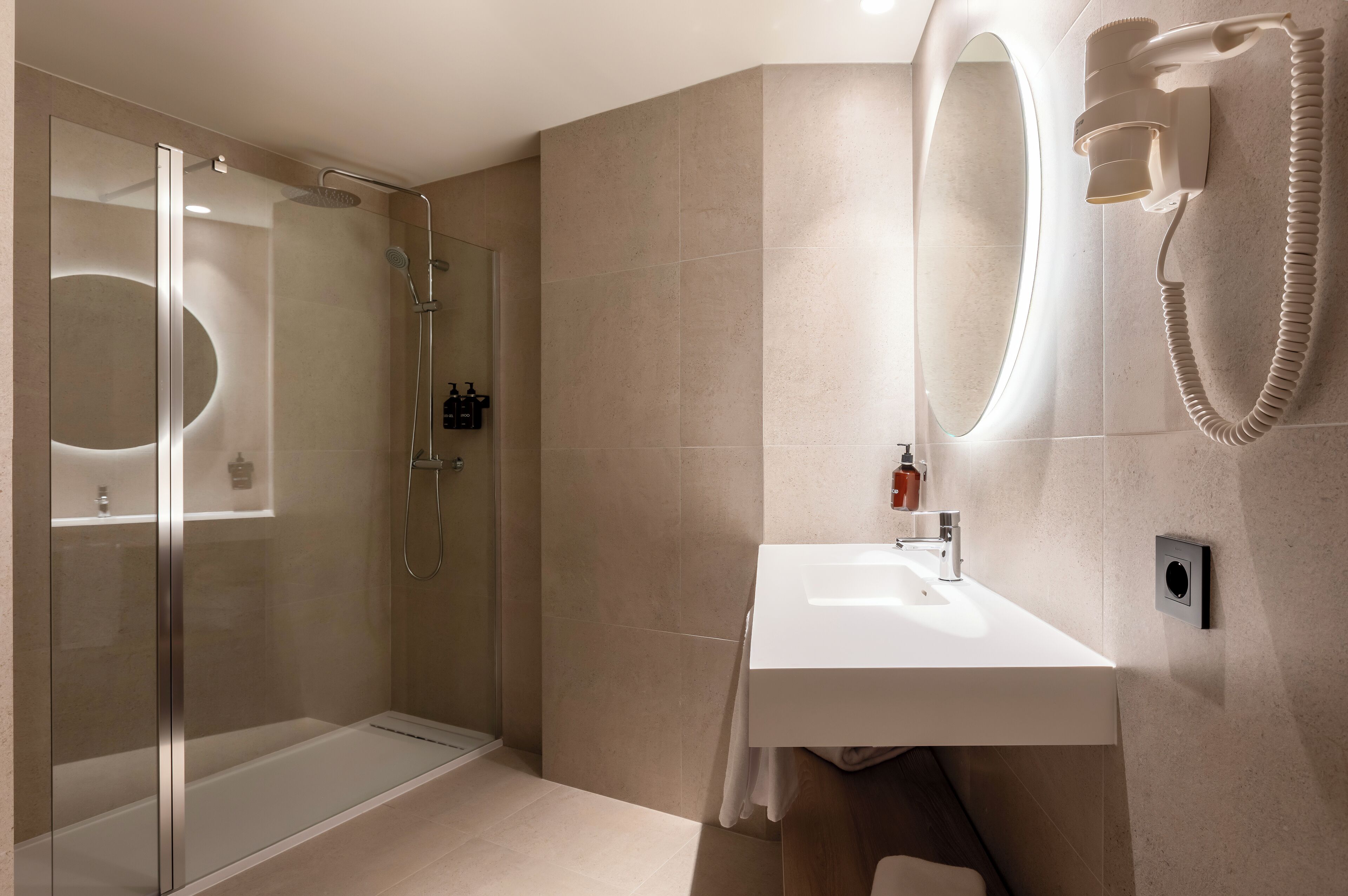 A modern bathroom with a glass-enclosed shower, a white sink, and a wall-mounted hairdryer.