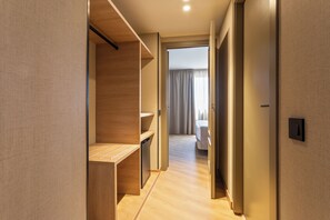En modern hotellkorridor med trägolv, inbyggda hyllor och ett synligt badrum med dusch och toalett.