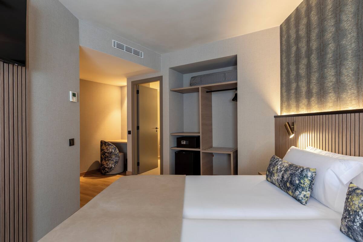 Una camera d'albergo con un letto, un armadio, una piccola scrivania e un lampadario a parete.