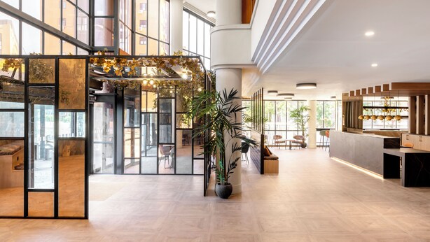 Een ruime lobby met grote ramen, een receptiebalie en een grote plant in het midden.