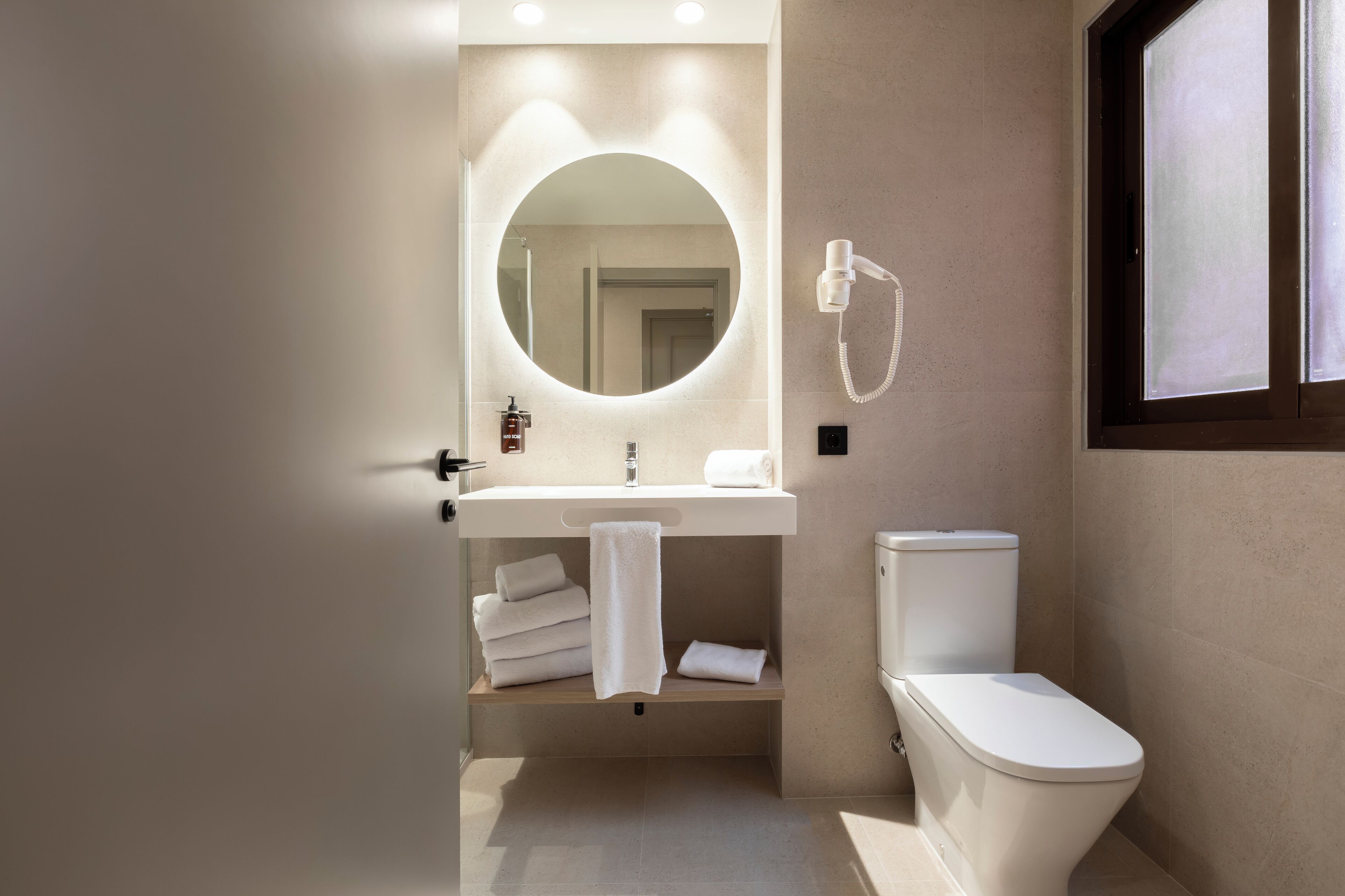 A modern bathroom with a round mirror, a white sink, a toilet, and a towel rack.