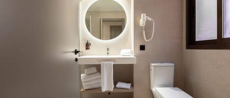 A modern bathroom with a round mirror, a white sink, a toilet, and a towel rack.