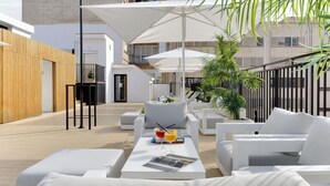 An outdoor lounge area with white furniture, umbrellas, and a magazine on a table. - Hotel Conqueridor (Valencia)