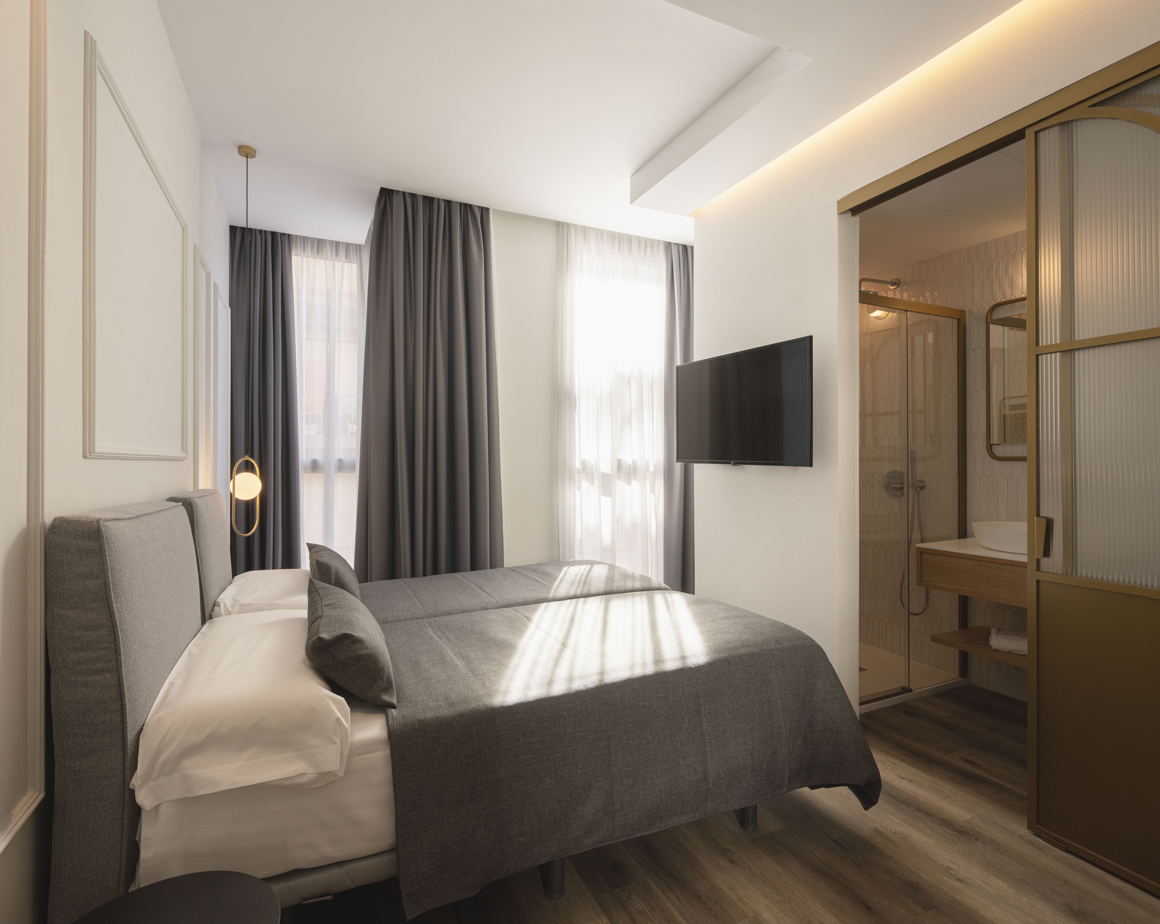 Una habitación de hotel moderna con cama, televisión, vestidor y zona de ducha.
