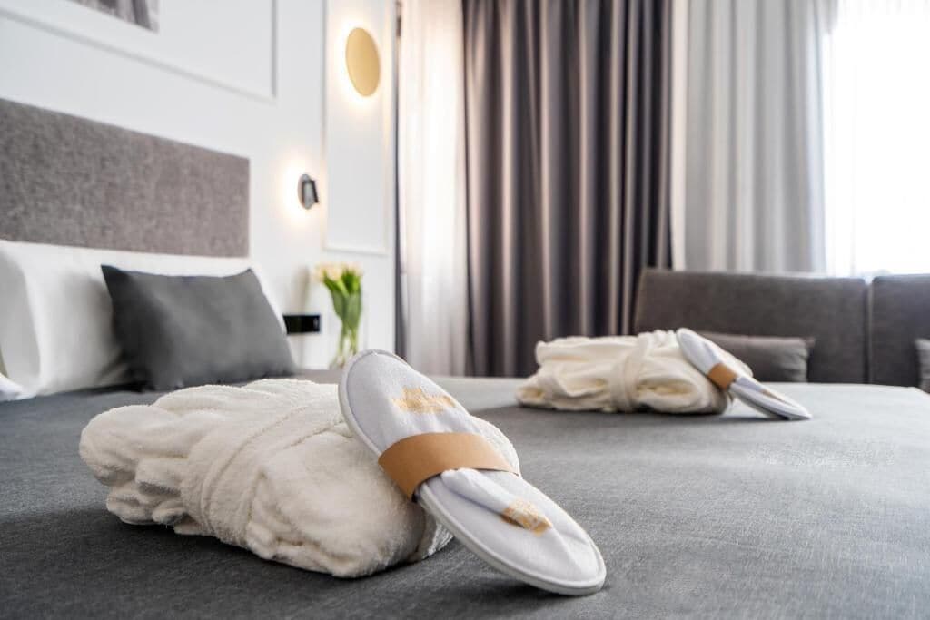 A hotel room with a neatly made bed, a grey sofa, and a wall-mounted light fixture.