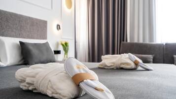 A hotel room with a neatly made bed, a grey sofa, and a wall-mounted light fixture.