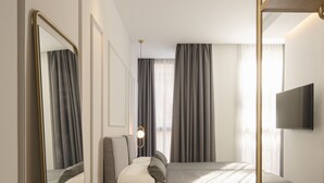A modern hotel room with a large bed, a sitting area with a small table, a mirror, and a TV mounted on the wall. - Hotel Conqueridor (Valencia)