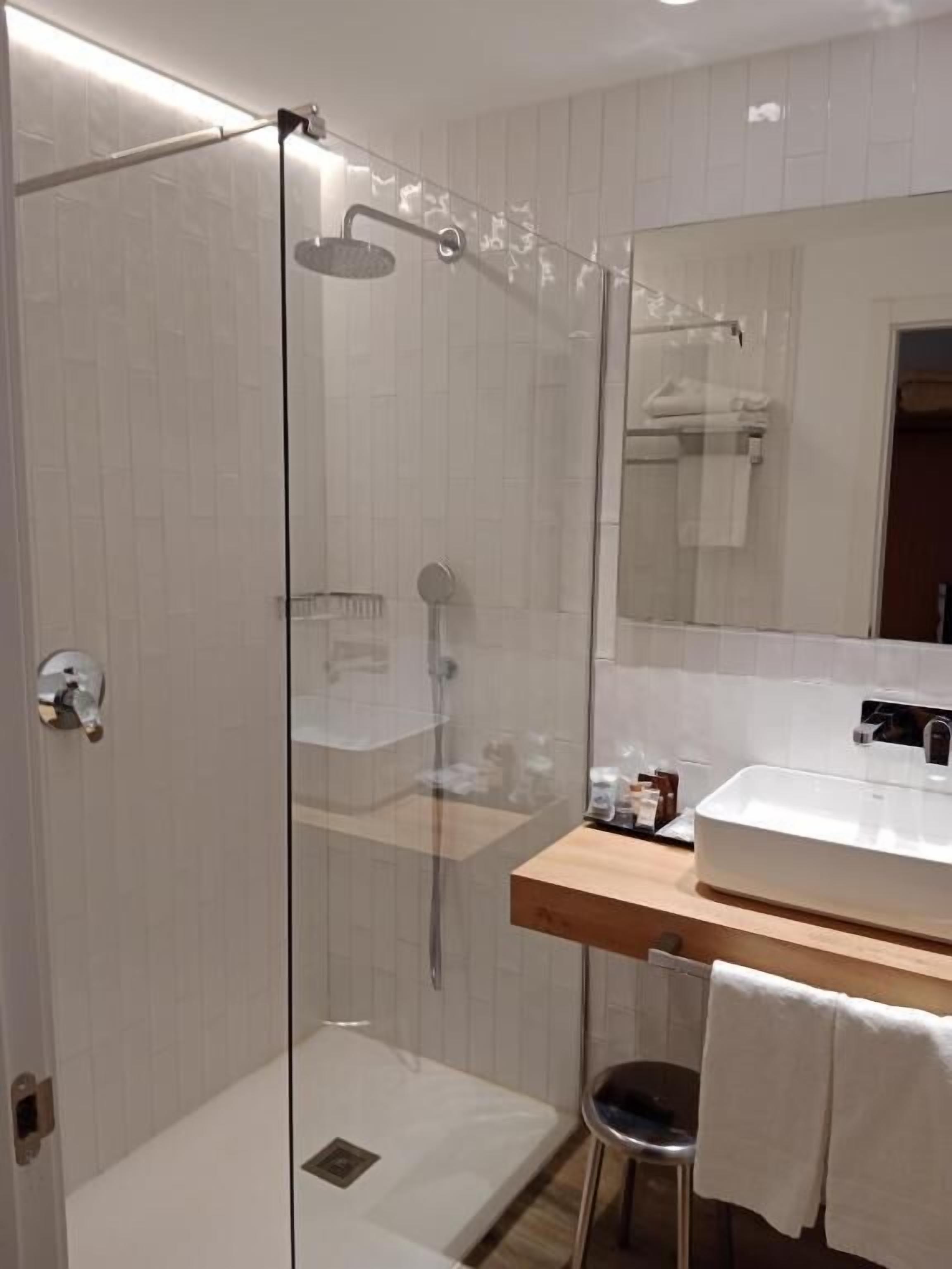 Un baño moderno con ducha de vidrio, lavabo blanco y espejo sobre el lavabo.