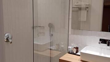 Un baño moderno con ducha de vidrio, lavabo blanco y espejo sobre el lavabo.