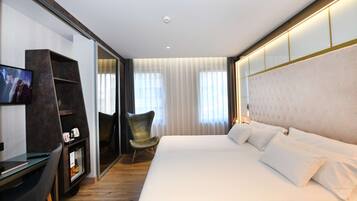 Una habitación de hotel moderna con una cama grande, un escritorio con computadora, un televisor y una silla.