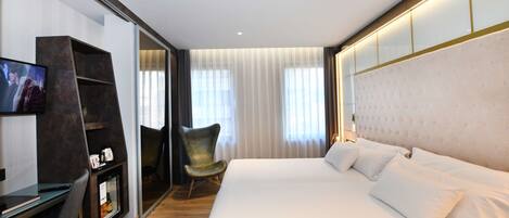 Una habitación de hotel moderna con una cama grande, un escritorio con computadora, un televisor y una silla.